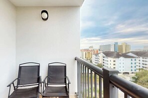 A balcony with two chairs and a railing, overlooking a cityscape with buildings. - Holiday Towers Unit 1001 (Myrtle Beach)