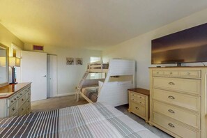 A bedroom with a bunk bed, a dresser, a television, and a door leading to another room. - Holiday Towers Unit 1001 (Myrtle Beach)