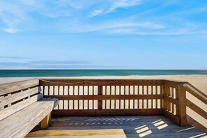 Ein hölzerner Steg führt zu einem Strand unter blauem Himmel.