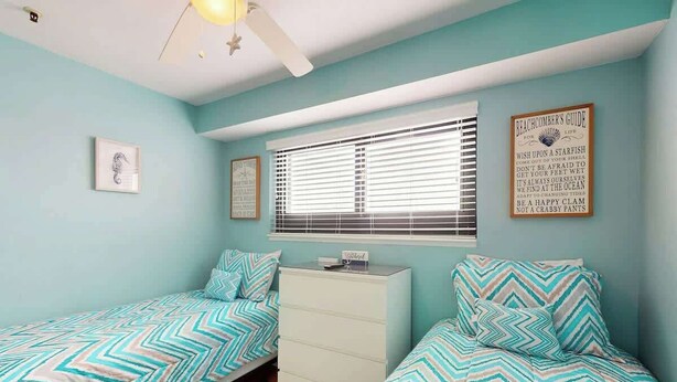 A bedroom with two single beds, a dresser, a window with blinds, and a wall with a framed sign. - Renaissance Tower 1114 (Myrtle Beach)