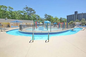 Ein Schwimmbecken mit einem umzäunten Spielbereich und Liegestühlen.
