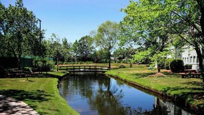 A serene park with a small bridge over a calm water body, surrounded by lush greenery and benches. - Renaissance Tower 1114 (Myrtle Beach)
