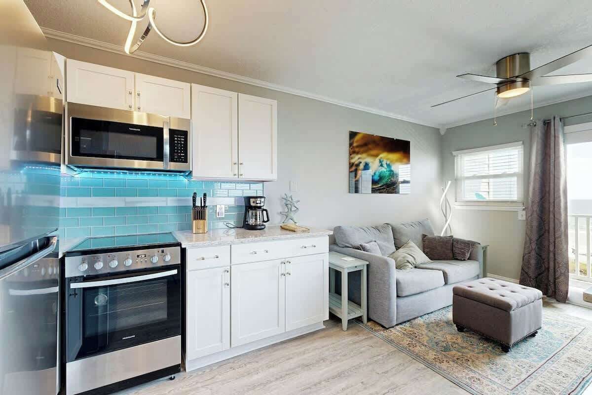 A modern kitchen with stainless steel appliances, a grey sofa, and a ceiling fan.