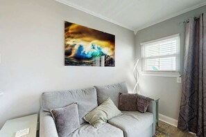 A room with a grey sofa, a painting of a wave, a window with blinds, and a patterned curtain. - Breathtaking Beach Views (North Myrtle Beach)