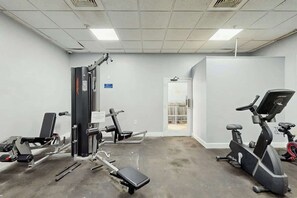 Ein Fitnessstudio mit Trainingsgeräten, darunter eine Langhantelbank, eine Beinpresse und ein Crosstrainer.