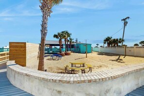 Een strandgebied met een houten terras, een palmboom en een klein gebouw met een blauw dak.