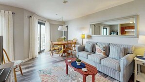 A living room with a sofa, a dining table with chairs, a TV, and a large mirror on the wall. - Renaissance Tower 816C (Myrtle Beach)