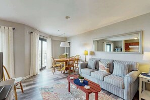 Ein Wohnzimmer mit einer Couch, einem Esstisch mit Stühlen, einem Fernseher und einem großen Spiegel an der Wand.