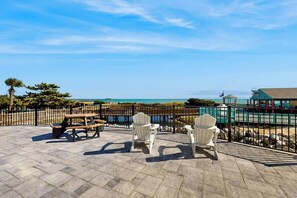 An outdoor patio with picnic tables and Adirondack chairs, overlooking a beach and ocean. - Renaissance Tower 816C (Myrtle Beach)