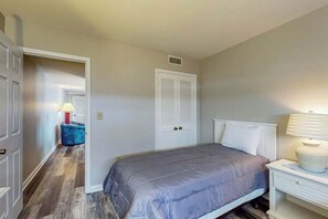 A bedroom with a bed, a nightstand, a lamp, a wardrobe, and a hallway leading to another room. - Renaissance Tower 816C (Myrtle Beach)