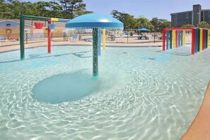 Ein Wasserspielbereich mit einer zentralen Fontäne und angrenzenden Spielgeräten.