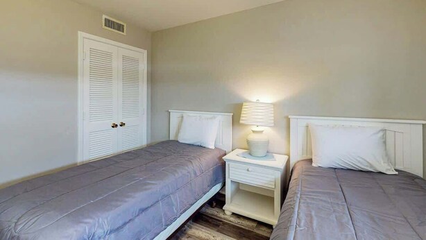 A bedroom with two beds, a white wardrobe, and a nightstand with a lamp. - Renaissance Tower 816C (Myrtle Beach)