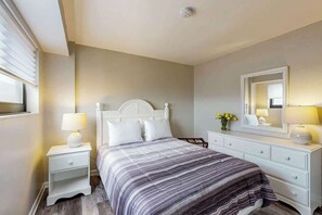Een slaapkamer met een bed, nachtkastje, dressoir en een spiegel.