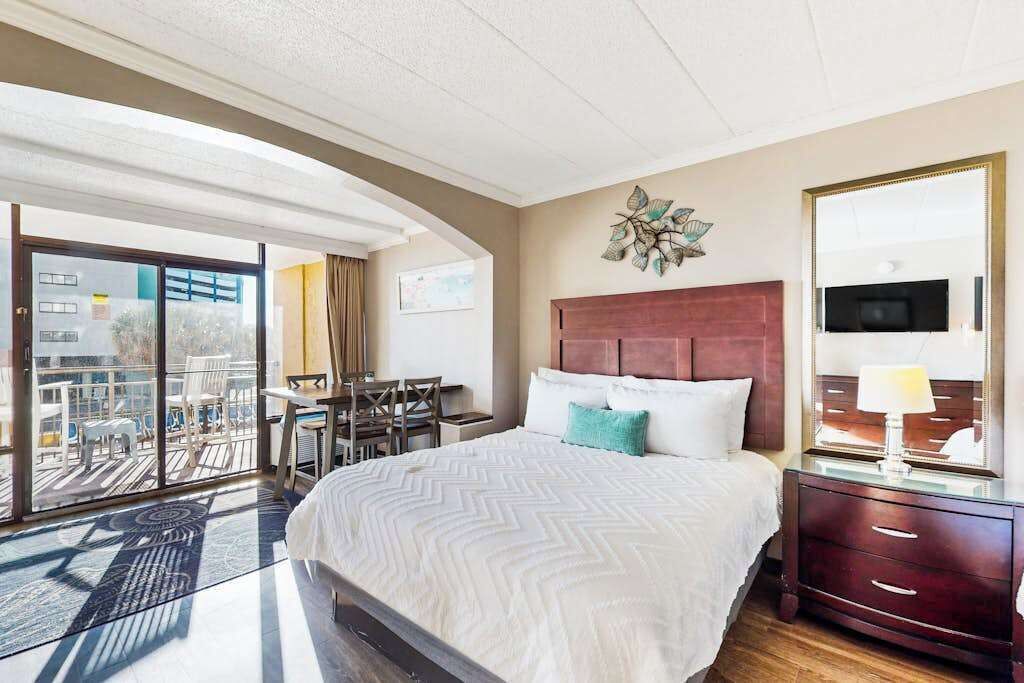 Une chambre d’hôtel avec un lit, un bureau, une chaise, une télévision et un balcon.