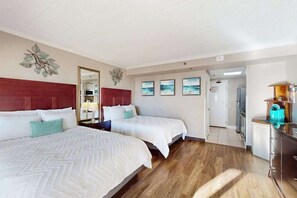 A hotel room with two beds, a wooden floor, a kitchen area, and a hallway leading to other rooms. - Caravelle Resort 206 (Myrtle Beach)
