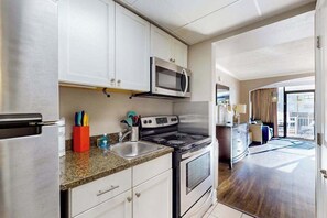 A modern kitchen with stainless steel appliances, white cabinetry, and a granite countertop. - Seaside Luxe | Caravelle Two Oh Six (Myrtle Beach)