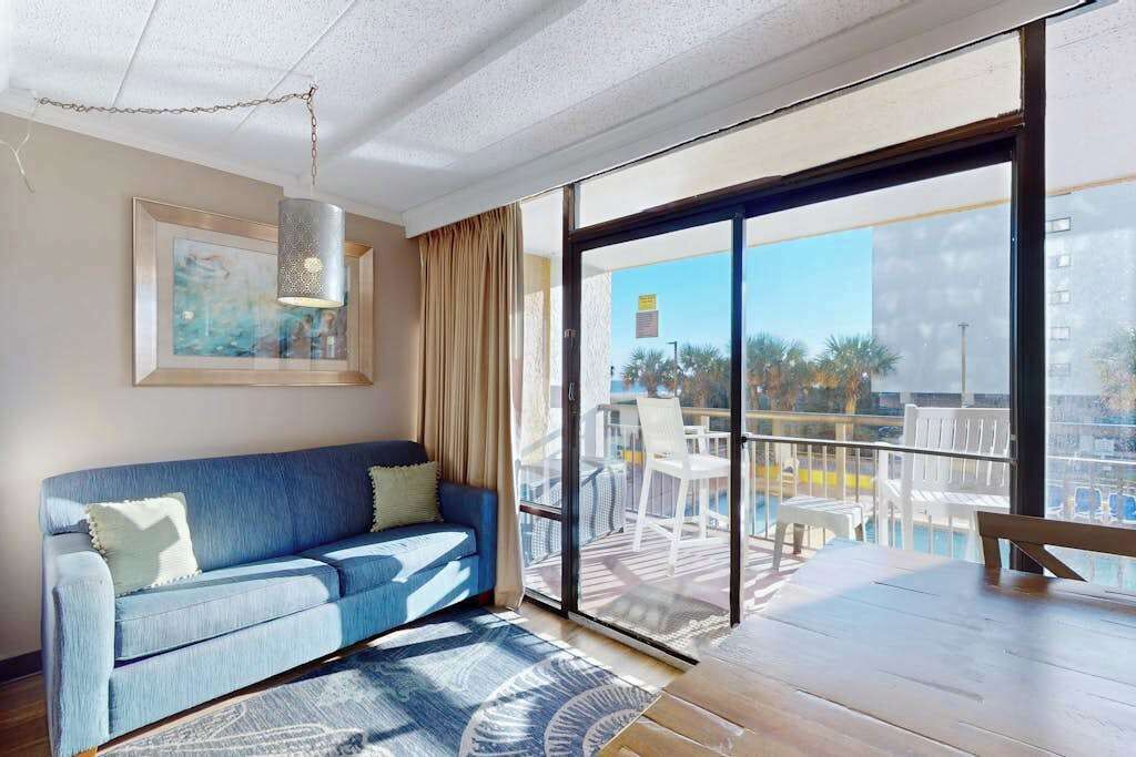 A room with a sofa, a dining table, and a balcony with outdoor furniture.