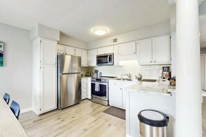 Une cuisine moderne avec des armoires blanches, des appareils en acier inoxydable et un plancher en bois.