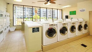Une buanderie équipée de plusieurs machines à laver, une pancarte indiquant « fermé » et une vue sur les bâtiments environnants.
