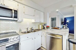 A modern kitchen with white cabinetry, a stainless steel microwave, a built-in oven, a dishwasher, and a marble countertop. - Myrtle Beach Resort A-544 (Myrtle Beach)