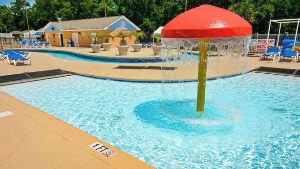 Une piscine agrémentée d’un élément décoratif aquatique, de chaises longues et d’un bâtiment en arrière-plan.