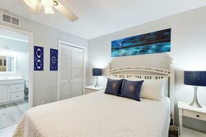 Une chambre d’hôtel avec un grand lit, une table de chevet, une lampe, un tableau au mur et une salle de bain avec un miroir et des placards.