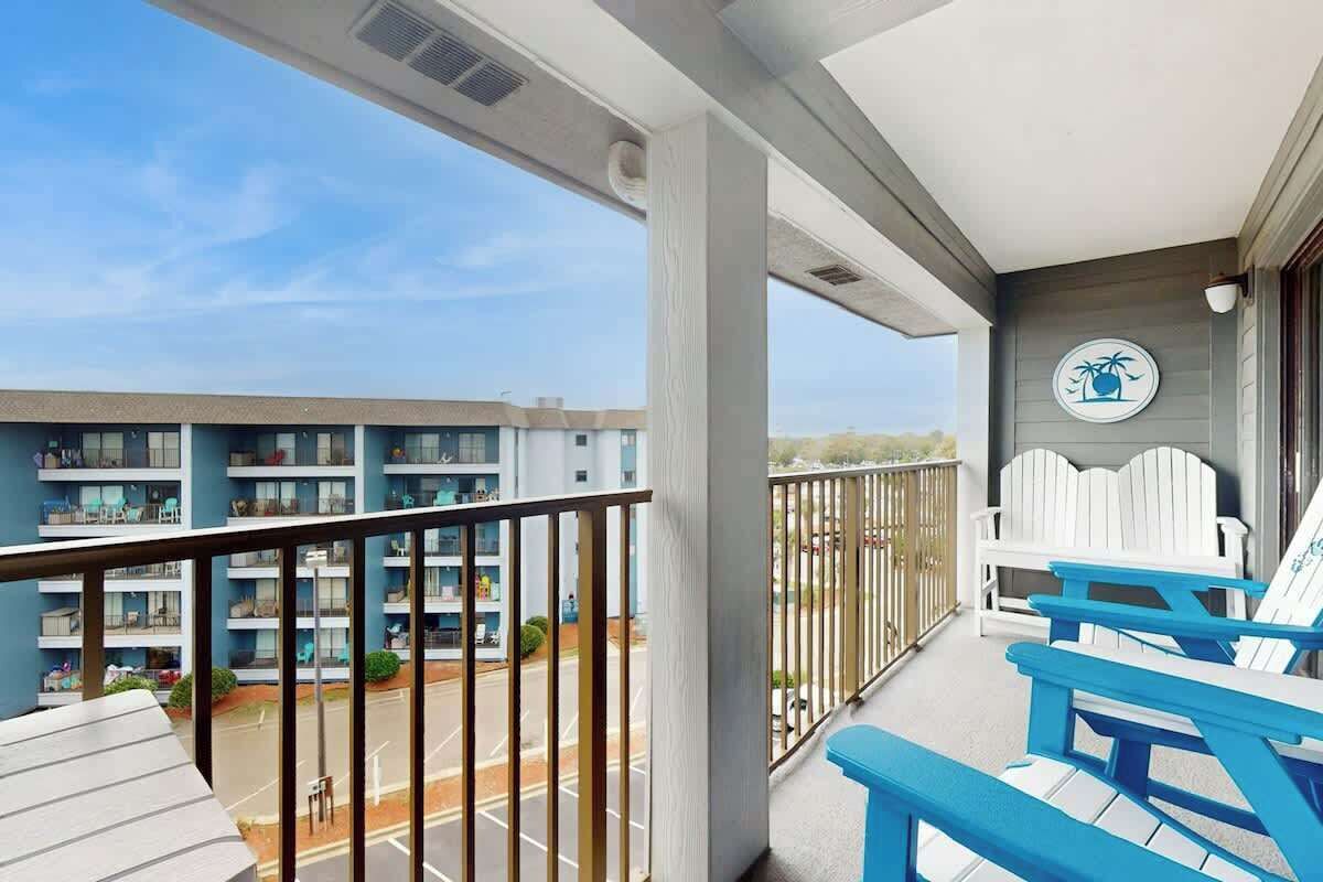 Un balcon donnant sur un parking et sur un immeuble à plusieurs étages. On y trouve deux chaises Adirondack blanches.