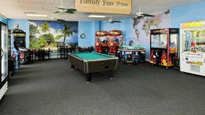 Un espace de loisirs familial avec une table de billard, des jeux d’arcade et une carte du monde affichée sur le mur.