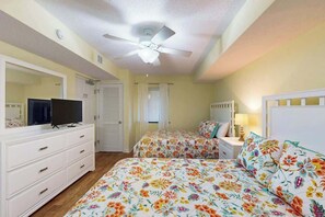 Ein Schlafzimmer mit zwei Betten, einem Deckenventilator, einem Fernseher auf einer Kommode und einem Nachttisch mit Lampe.