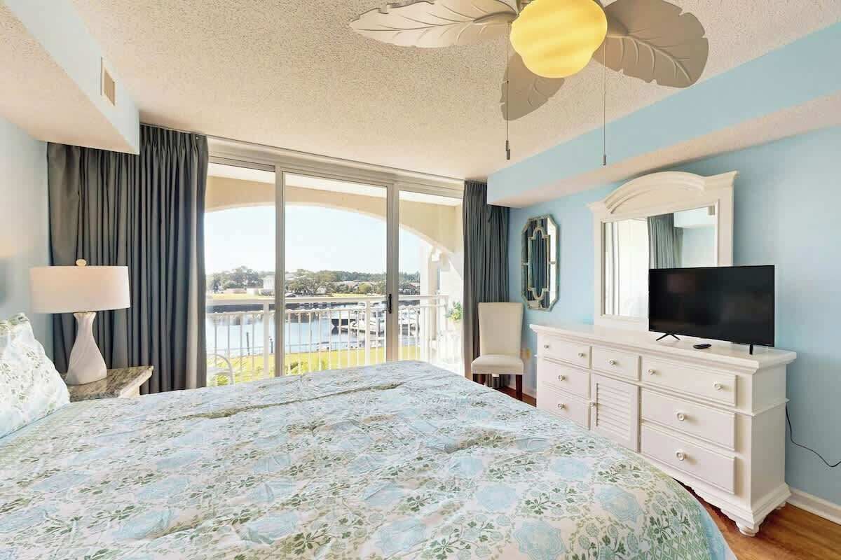 Une chambre à coucher avec un lit, une commode, une télévision et un balcon offrant une vue.