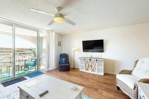 Ein Wohnzimmer mit Balkon, Deckenventilator, Flachbildfernseher, Rattan-Sofa und einem weißen Schrank.