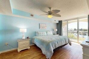 Un dormitorio con cama, mesita de noche, lámpara, ventilador de techo y un amplio ventanal con vistas.