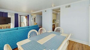 A room with a dining table, chairs, a sofa, and a television. - Ocean Bridge Unit 4-B19 (Myrtle Beach)