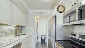 A kitchen with white cabinets, a stainless steel microwave, a dishwasher, and a clock on the wall. - Ocean Bridge Unit 4-B19 (Myrtle Beach)