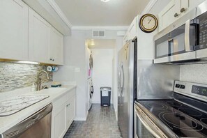 A kitchen with white cabinets, a stainless steel microwave, a dishwasher, and a clock on the wall. - Ocean Bridge Unit 4-B19 (Myrtle Beach)