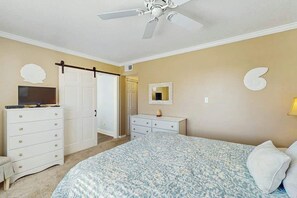 A bedroom with a bed, a dresser, a television, a ceiling fan, and a door leading to another room. - Ocean Bridge Unit 4-B19 (Myrtle Beach)