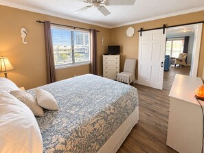 A hotel room with a bed, a desk, a chair, a dresser, a television, and a sliding door leading to another room. - Ocean Bridge Unit 4-B19 (Myrtle Beach)