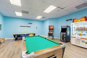 A pool table with a green felt surface, a blue pool table in the background, and arcade machines on the right. - Renaissance Tower 915 (Myrtle Beach)