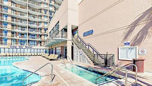 A pool area with multiple swimming pools, lounge chairs, and a staircase leading to an upper deck. - Grande Cayman Unit 1057 (Myrtle Beach)