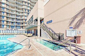 Ein Poolbereich mit mehreren Schwimmbecken, Liegestühlen und einer Treppe zu einem erhöhten Deck.