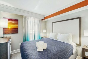 Ein Hotelzimmer mit einem großen Bett, einem Nachttisch, einem Schreibtisch und einem Gemälde von einem Sonnenuntergang.