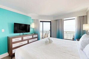 Ein Hotelzimmer mit einem großen Bett, einem Fernseher, einem Schminktisch und einem Balkon mit Vorhängen.