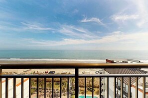 A view from a balcony overlooking a beach with a pool and a building in the foreground. - Grande Cayman Unit 1057 (Myrtle Beach)