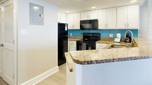 A modern kitchen with white cabinets, a black refrigerator, a microwave, and a granite countertop. - Grande Cayman Unit 1057 (Myrtle Beach)