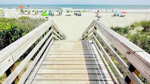 A wooden boardwalk leading to a beach with umbrellas and chairs. - Monterey Bay Unit 823 (Myrtle Beach)