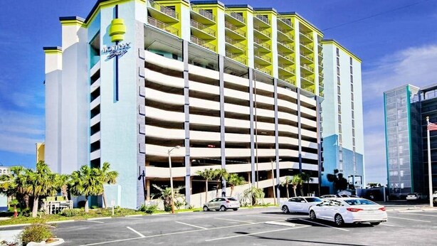 A multi-story parking garage with a hotel sign, surrounded by palm trees and a clear sky. - Monterey Bay Unit 823 (Myrtle Beach)