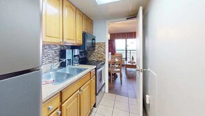 A compact kitchen with wooden cabinets, a built-in microwave, and a large window. - Monterey Bay Unit 823 (Myrtle Beach)