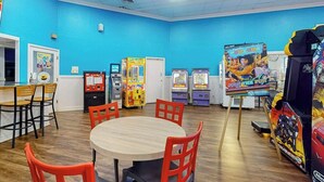 Um quarto com paredes azuis, uma mesa de madeira com cadeiras e vários jogos de fliperama.
