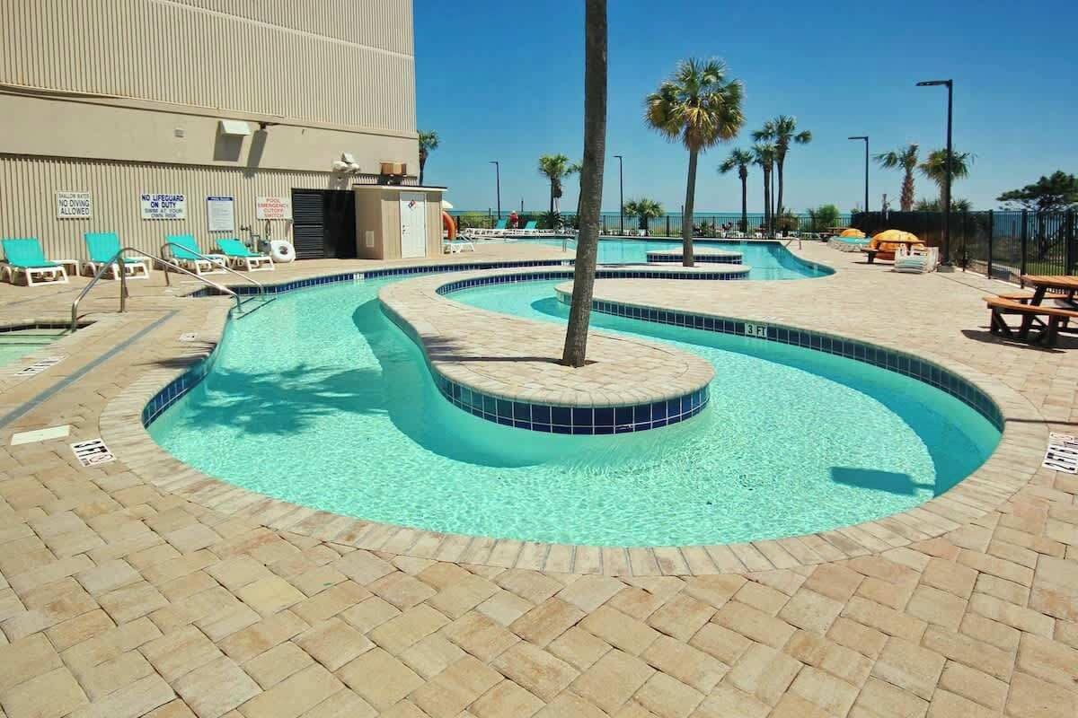 A swimming pool with a curved design, surrounded by lounge chairs and palm trees.