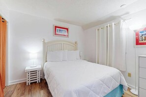 A bedroom with a bed, a nightstand, a wall-mounted picture, and a window with curtains. - Myrtle Beach Resort B-446 (Myrtle Beach)